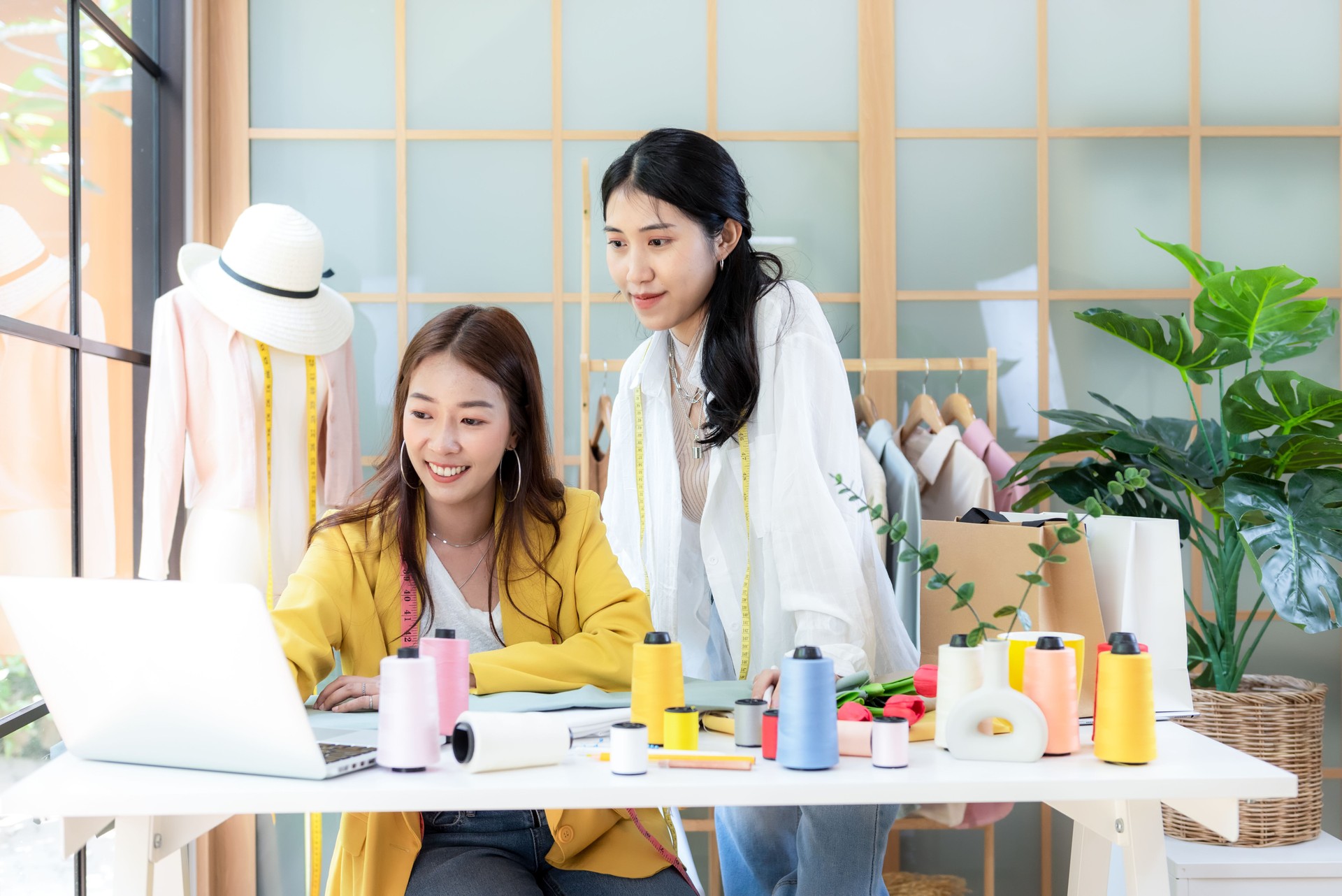 Two young women fashion designer  working on her designer in the showroom.  Lifestyle Stylish tailor use computer clothing design in studio.  Business small Concept